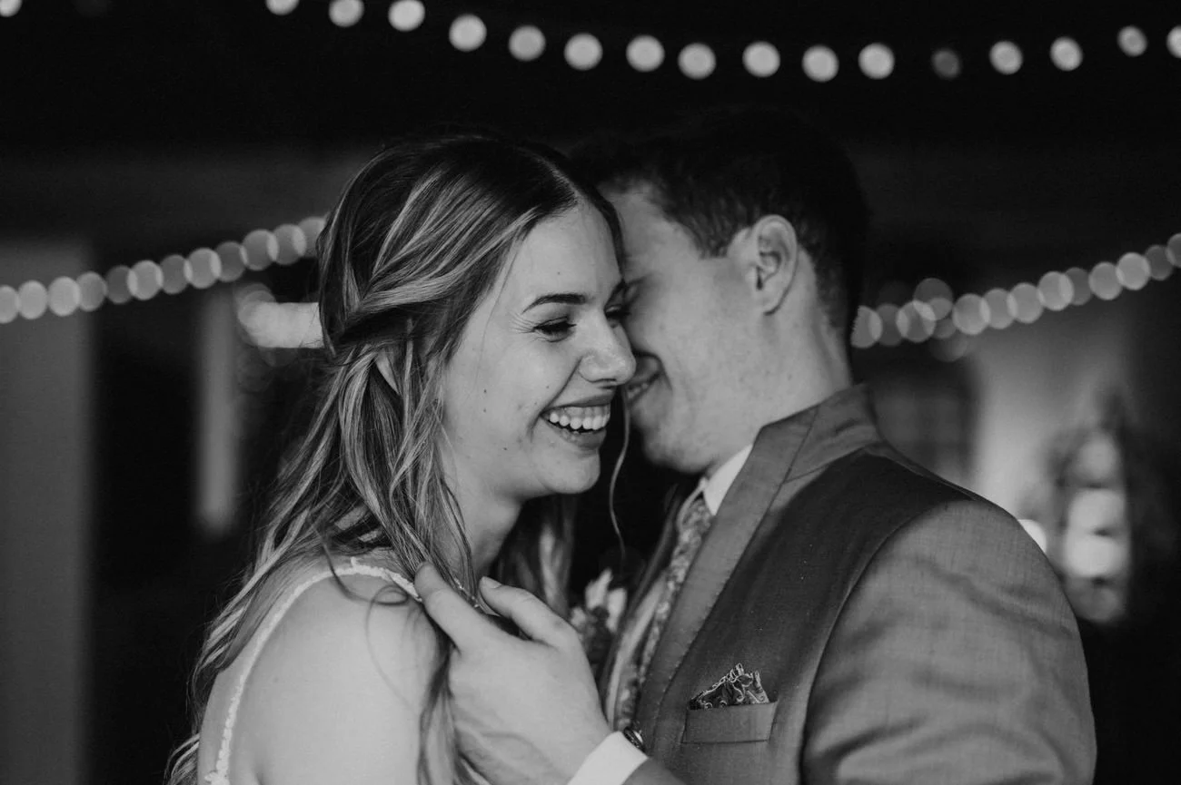 Ein Schwarz-Weiß Bild von einem Brautpaar. Der Bräutigam flüstert der Braut was ins Ohr - die Braut lacht.